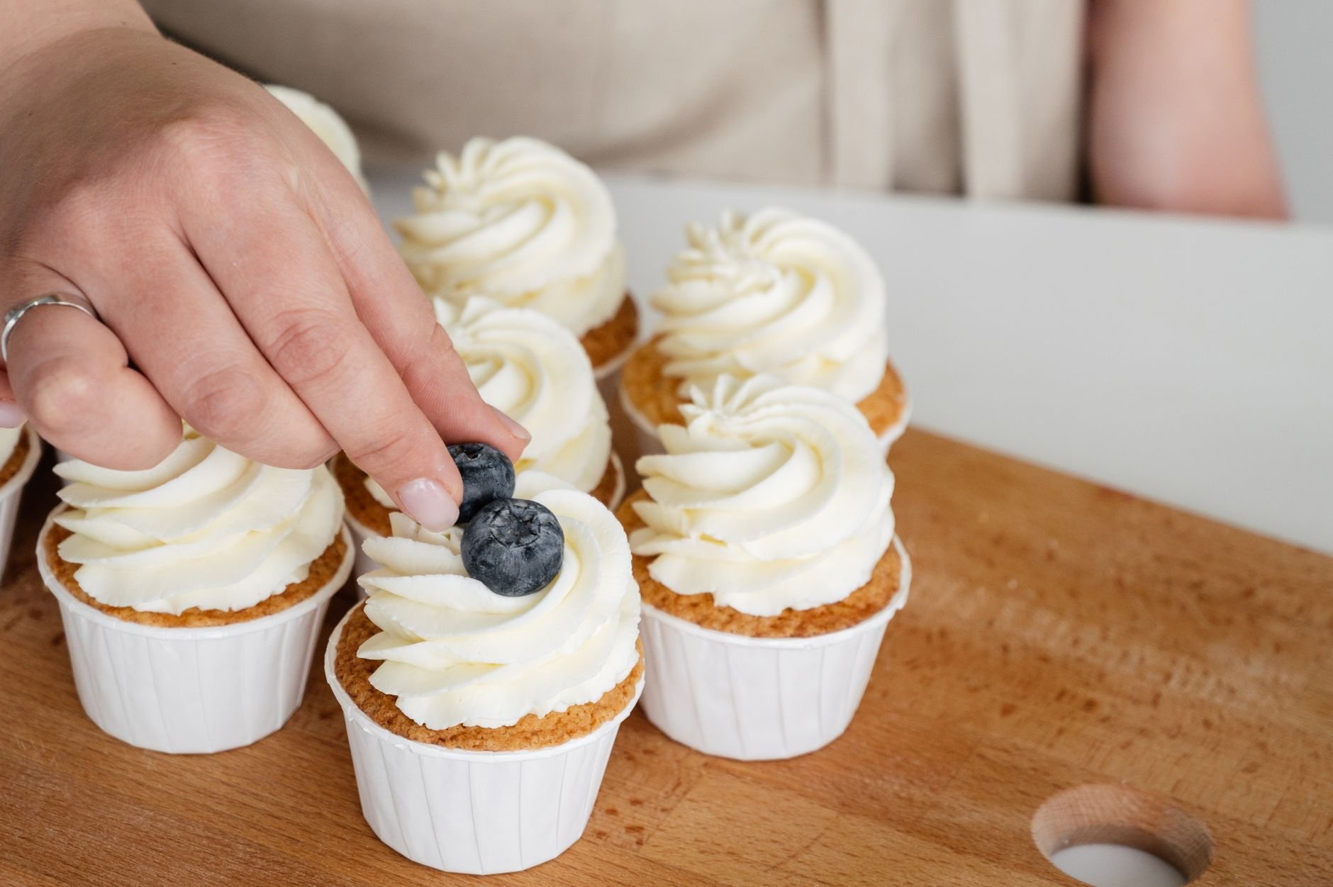 Close-up of hands carefully decorating a cupcake with fresh toppings.